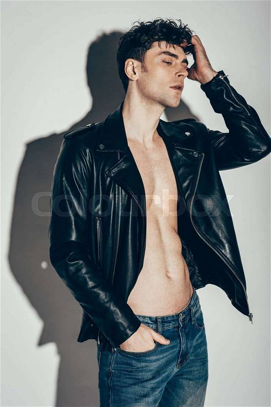 Handsome sexy man posing in jeans and black leather jacket on grey, stock photo