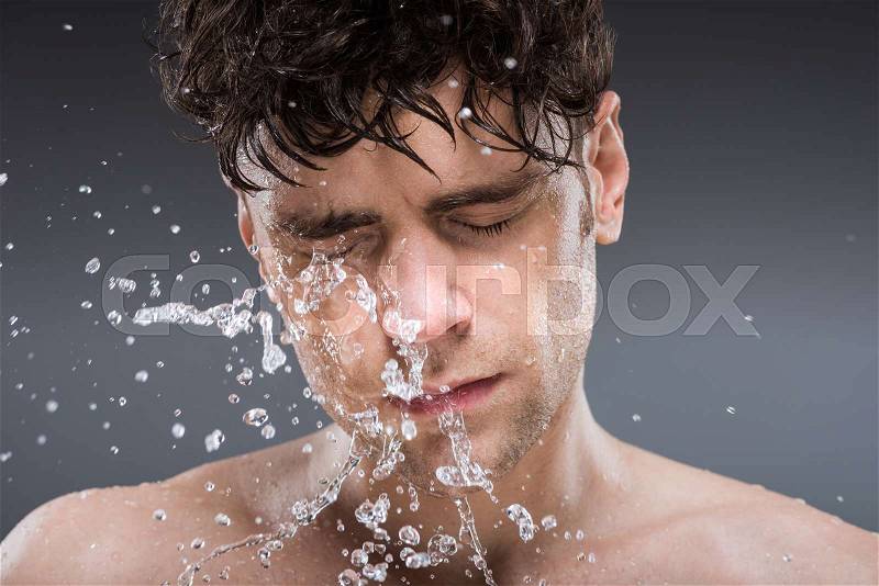 Handsome man washing face with water in the morning, isolated on grey, stock photo