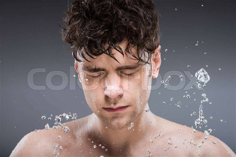 Young man washing face with water, isolated on grey, stock photo