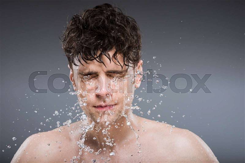 Handsome man washing face with water drops, isolated on grey, stock photo