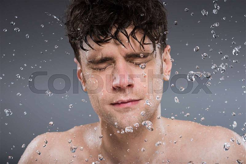 Handsome man washing face with water, isolated on grey, stock photo