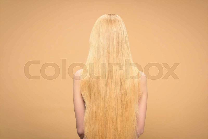 Back view of long-haired blonde woman standing on beige background, stock photo