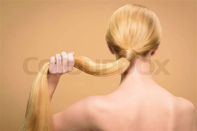 Back view of naked blonde woman holding long straight hair isolated on beige, stock photo