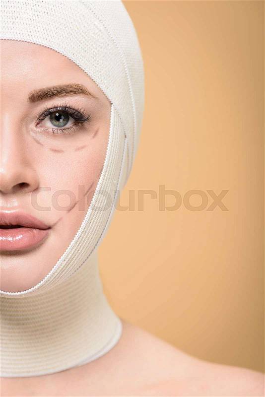 Cropped shot of woman with bandages over head and correcting marks on face looking at camera isolated on beige, stock photo