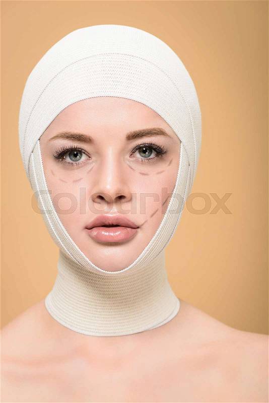 Young woman with bandages over head and lines on face looking at camera isolated on beige, stock photo