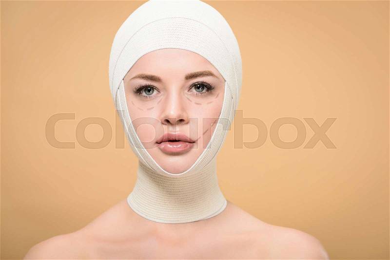 Young woman with bandages over head and marks on face looking at camera isolated on beige, stock photo