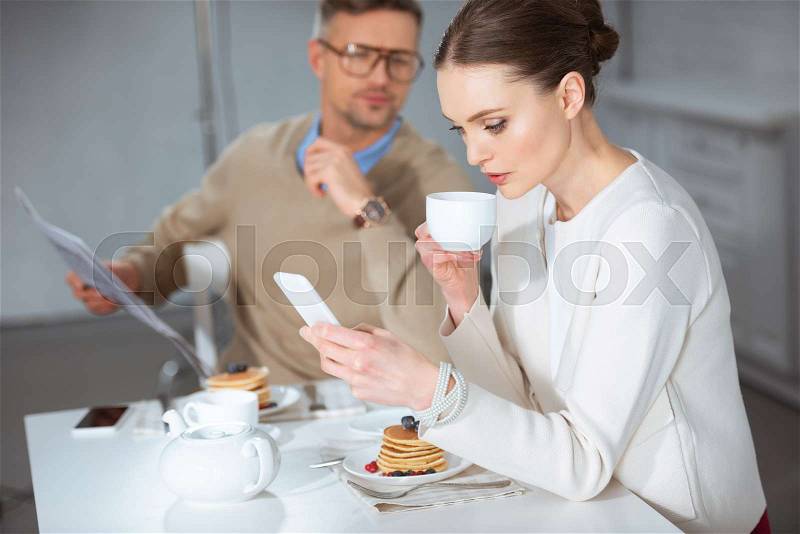 Woman using smartphone and ignoring man during breakfast in morning, stock photo