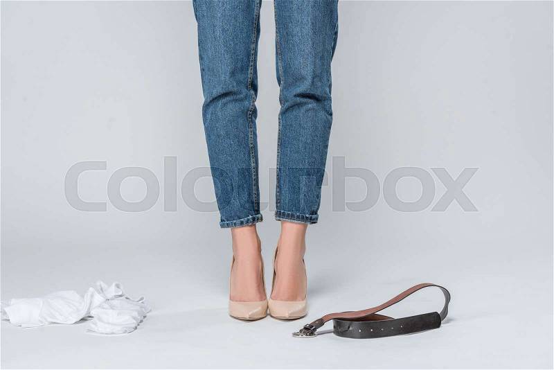 Low section view of woman in jeans and high heels undressing isolated on grey , stock photo