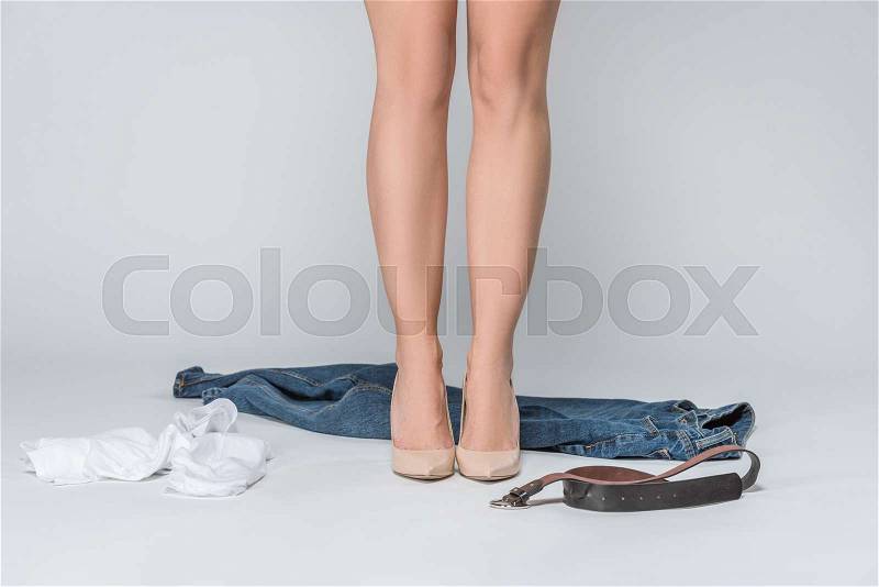 Low section view of woman in high heels undressing isolated on grey , stock photo
