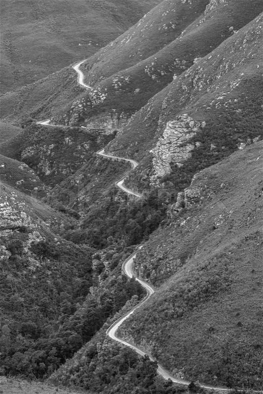 High rugged old dirt road pass through rugged mountains in black and white landscape, stock photo