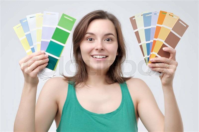 Young european woman in green clothes select a color to paint her wall. She is glad to have such a variety of choice, stock photo