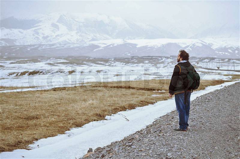 Touris wearing backpack and standing at the rural road while looking at the winter mountains, stock photo