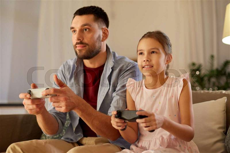 Family, gaming and entertainment concept - happy father and little daughter with gamepads playing video game at home in evening, stock photo
