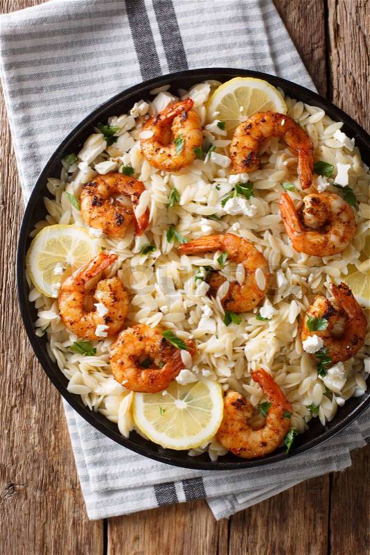 Orzo pasta with grilled shrimps, feta cheese and lemon close-up on a plate on the table. Vertical top view from above, stock photo