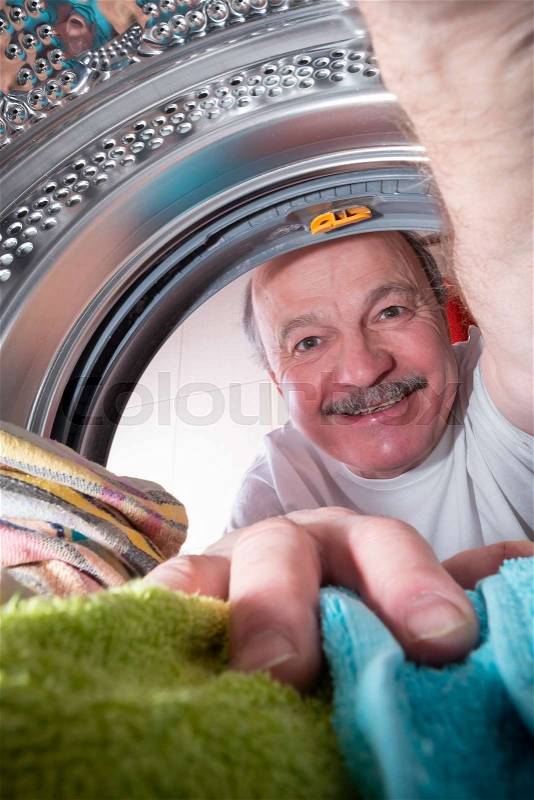 Senior man putting dirty towels in washing machine to clean them. View from washing machine inside. Everyday chore concept, stock photo