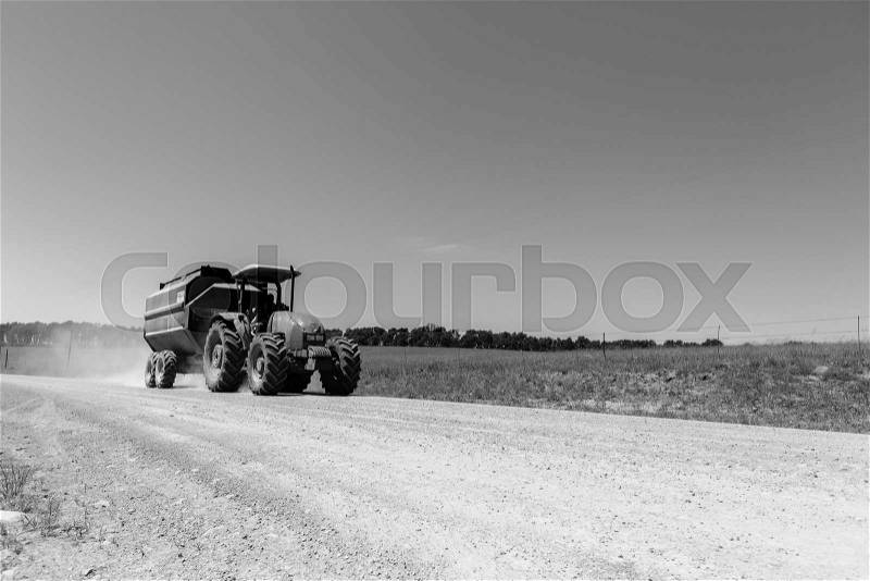Tractor trailer driver on dirt road in rural black and white mountains farming landscape, stock photo