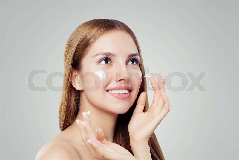 Healthy young woman with clear skin applying moisturizing cream on white background with copy space, stock photo