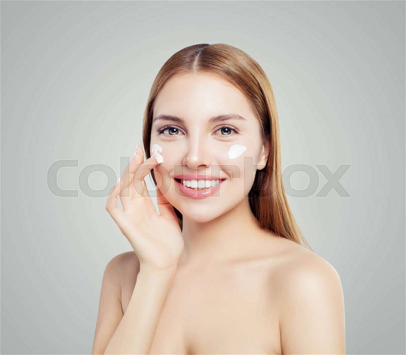 Cheerful female model applying anti-aging cream on her face. Skin care, beauty and facial treatment concept, stock photo