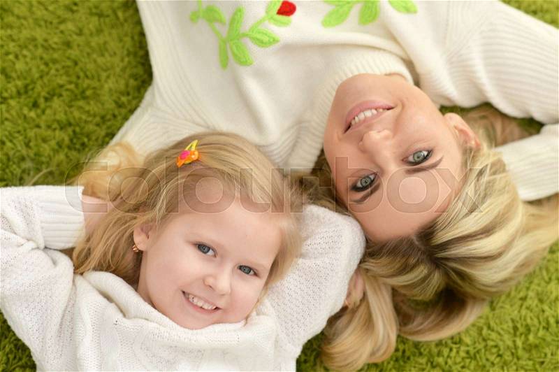 Mother with little daughter lying on green carpet at home, stock photo