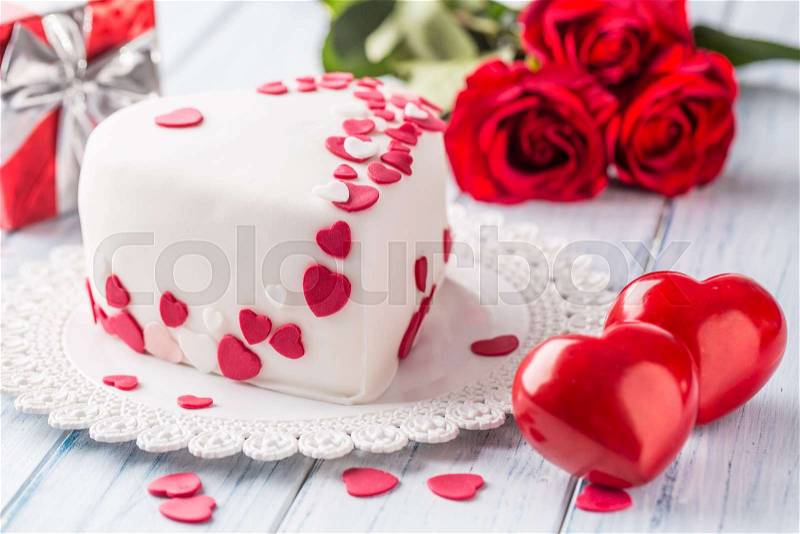 Marzipan white cake in the shape of a heart with red hearts. As the decoration bouquet of red roses a gift from the ribbon. Wedding or valentines day concept, stock photo