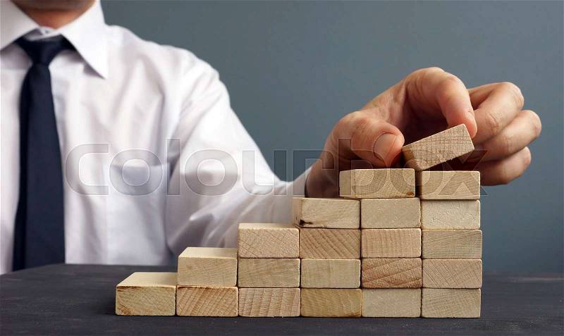 Success in business and career. Man rises figurine on a ladder from wooden blocks. Achievement, stock photo
