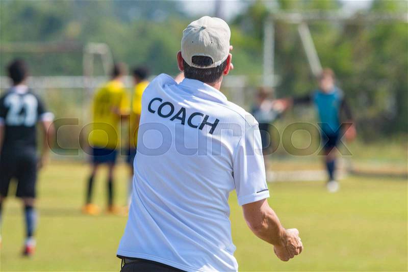 Back view of male football coach in white COACH shirt at an outdoor football field giving direction to his football team, stock photo