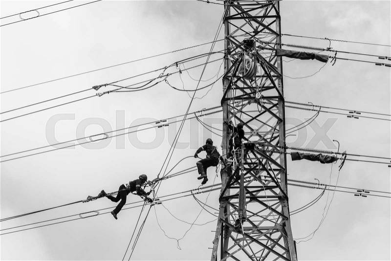 Electricians hanging on steel cables high above ground working on electrical cable power lines on steel tower black and white photo, stock photo