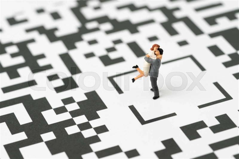 Couple or family life in digital age idea concept, miniature figurine couple man holding woman with love standing at the center of confusing QR code labyrinth maze, stock photo