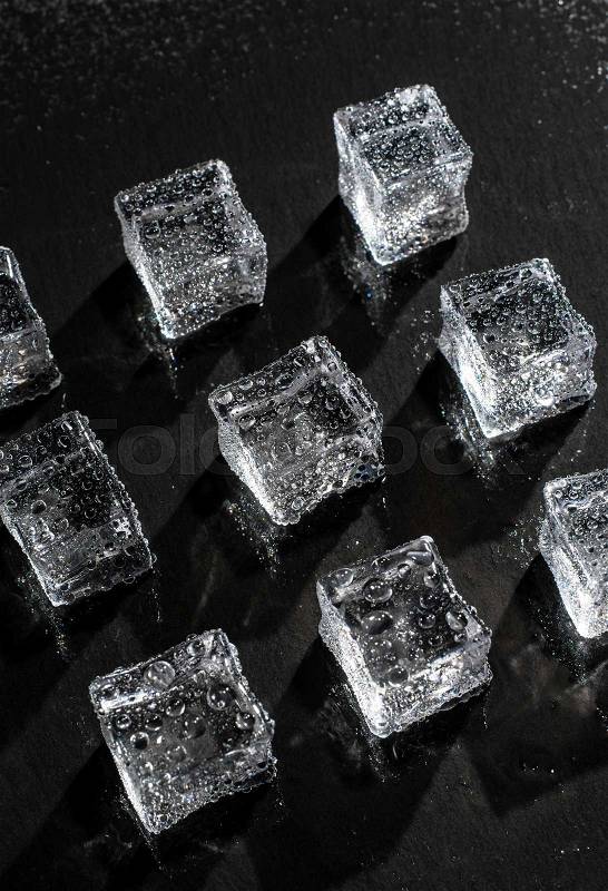 Ice cubes on black stone board. Wet ice cubes with water drops. Hard light. Deep shadows. Cold and freshness concept. Summer drinks conceptions. Dark background, stock photo