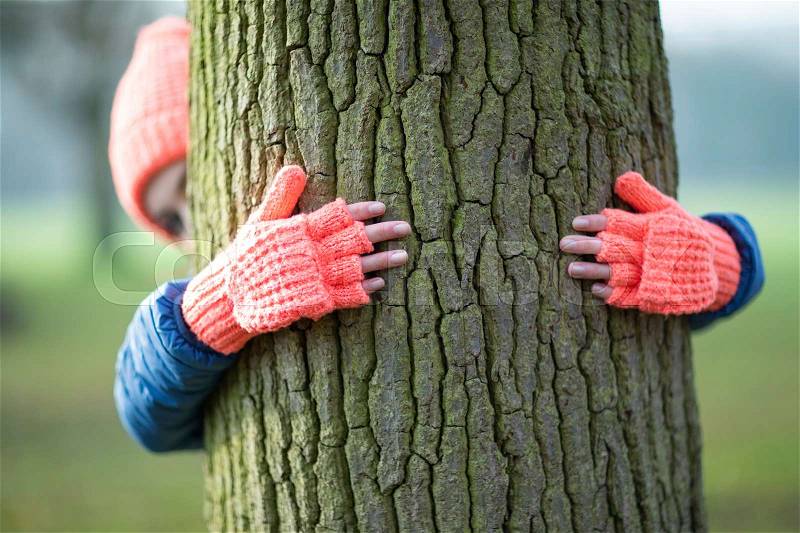 Woman Wearing Gloves Hugging Tree Trunk On Winter Walk In Countryside, stock photo