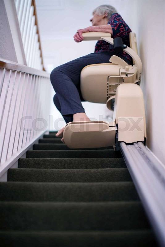 Senior Woman Sitting On Stair Lift At Home To Help Mobility, stock photo