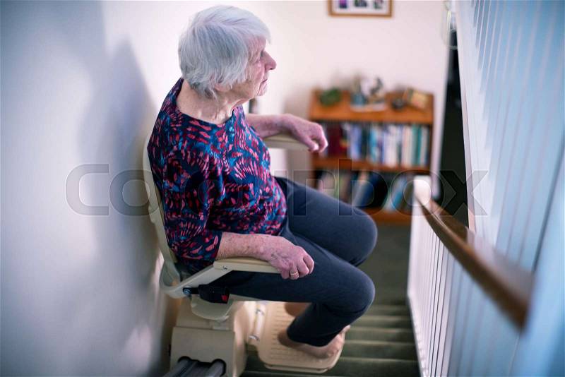 Senior Woman Sitting On Stair Lift At Home To Help Mobility, stock photo