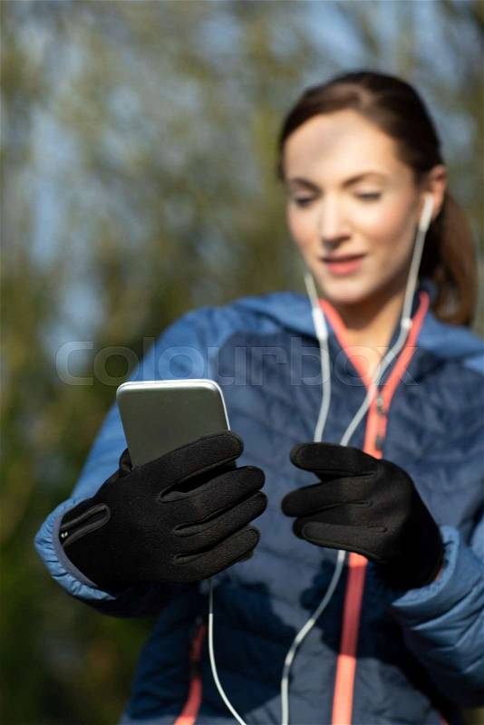 Young Woman Choosing Music To Listen To On Mobile Phone Before Exercising In Park, stock photo
