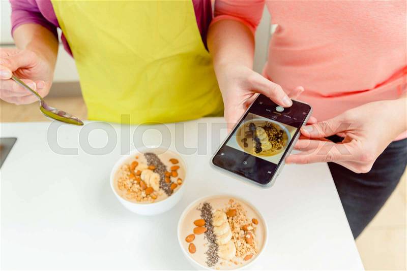 Female food blogger takes pic of healthy oatmeal bowls for blog through cellphone, stock photo