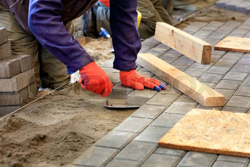 The worker levels the platform for laying paving slabs with the help of a trowel and wooden bars, aligning it to the level of the tensioned thread, stock photo