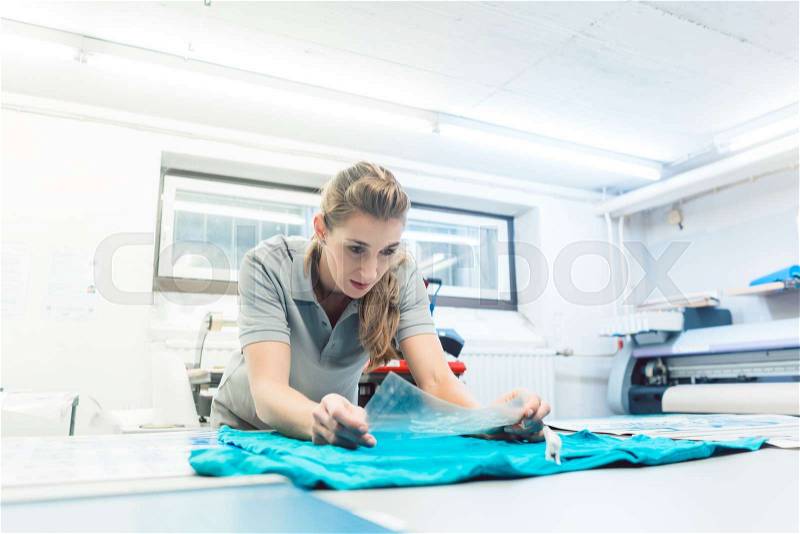 Woman flock printing a T-shirt as promotional item in workshop , stock photo
