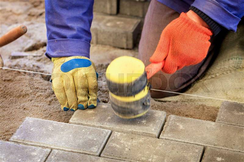 The worker lay the paving slab with special hammers, leveling it according to the level of the tensioned thread, stock photo