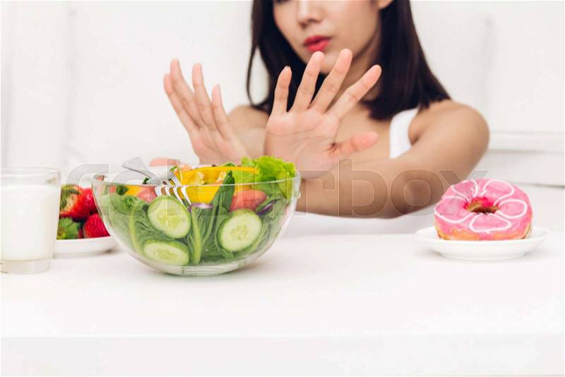 Woman making choice between healthy salad and calorie bomb chocolate donut.Woman rejecting with salad at home.Healthy eating diet and Junk food concept, stock photo