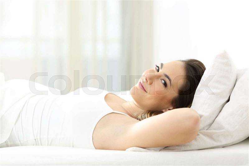 Satisfied guest lying on the bed looking at camera in an hotel room, stock photo