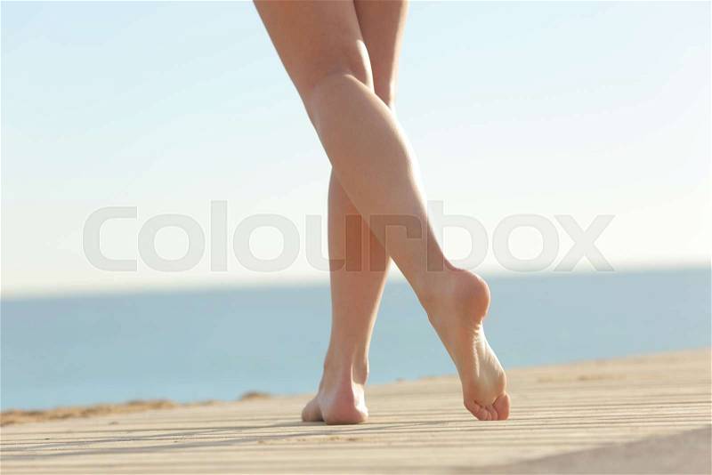 Close up of a woman waxed legs walking on the beach on a wooden floor, stock photo