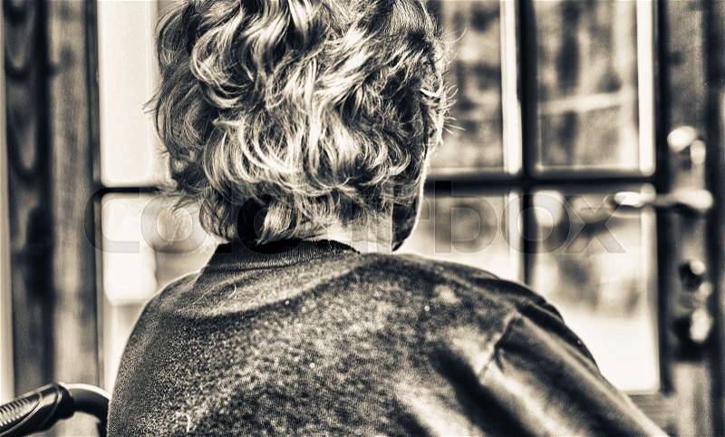 Elderly woman looking towards the window at home, stock photo
