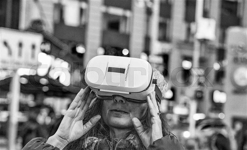 Close up of woman using virtual reality simulator against blurry Manhattan street at night, stock photo