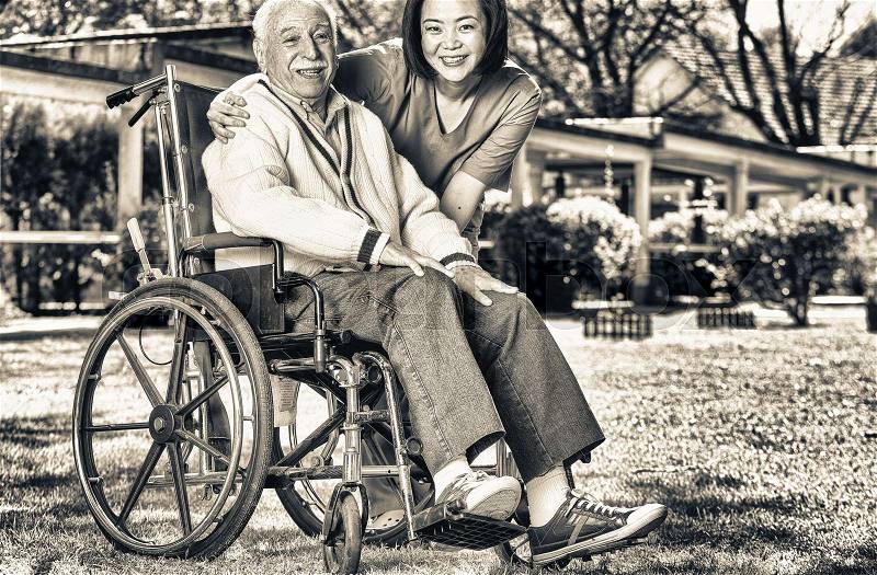 Asian and african nurses helping elder man on wheelchair at rehab facility garden, stock photo