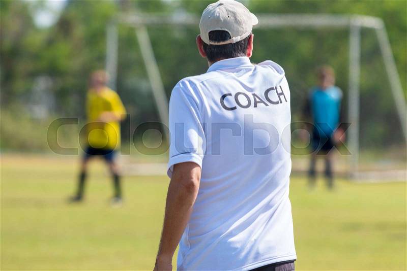 Back of male football coach wearing white COACH shirt talking to his football team giving them game direction at an outdoor football field, stock photo