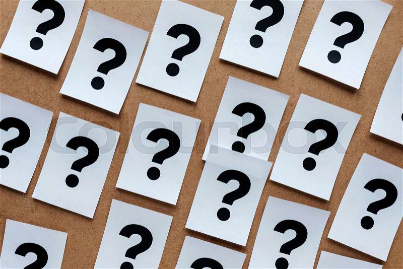 Bold black question marks on paper cards scattered randomly over a wooden background in a conceptual image, stock photo