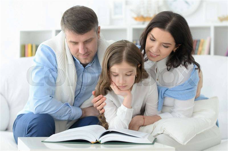 Parents and daughter reading big book in room at home, stock photo