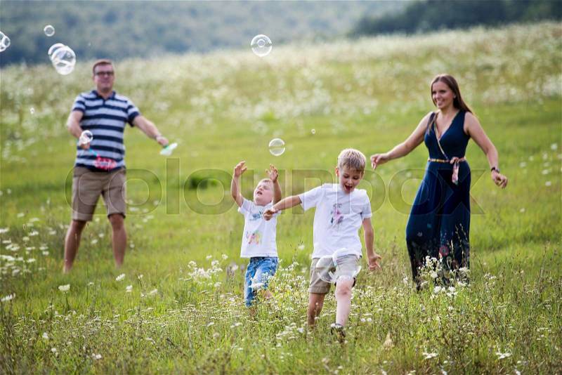 A young family with two small cheerful sons walking in nature on a summer day, blowing soap bubbles, stock photo