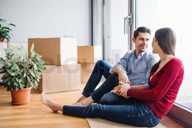Young couple in love moving in a new home, sitting on the floor and looking at each other, stock photo