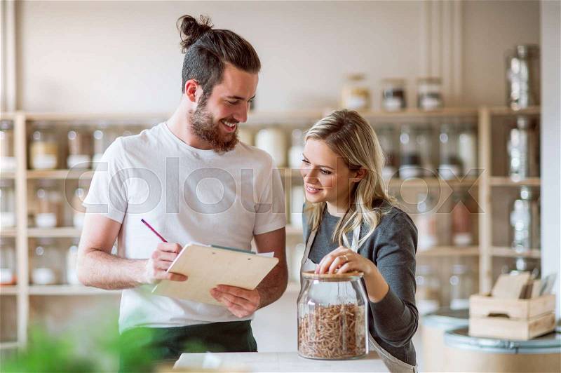 Two shop assistants standing in zero waste shop, checking and ordering stock, stock photo