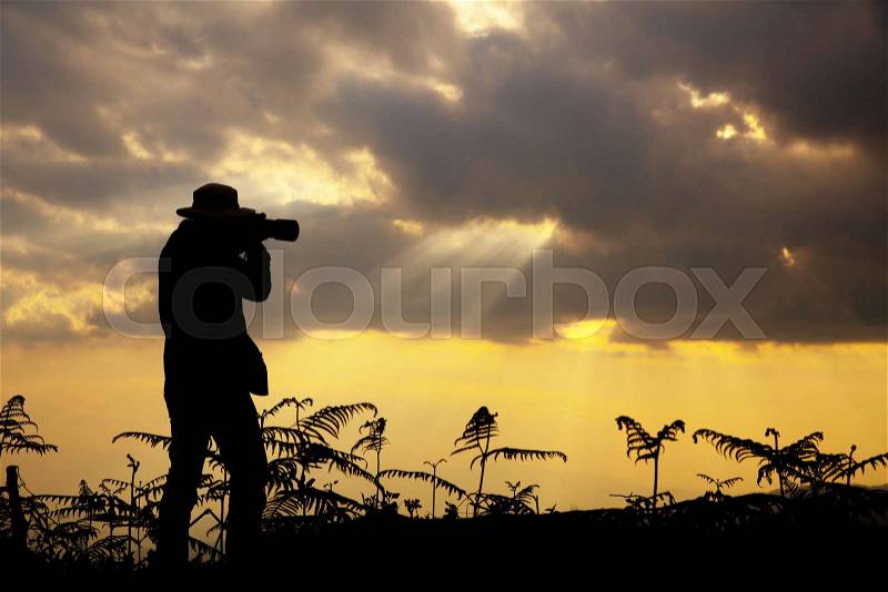 Silhouette of a photographer who shoots a sunset in the mountains, stock photo